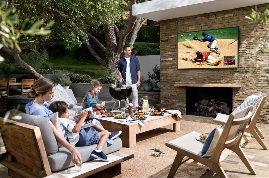 A family enjoying a cookout while watching a baseball game on their outdoor TV.