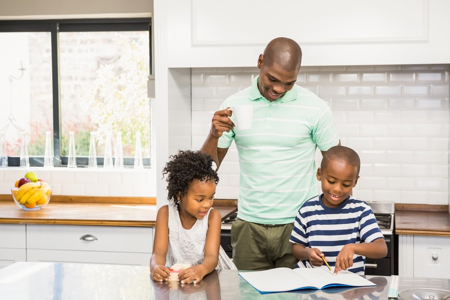 A man and two children at a kitchen counter reviewing school work