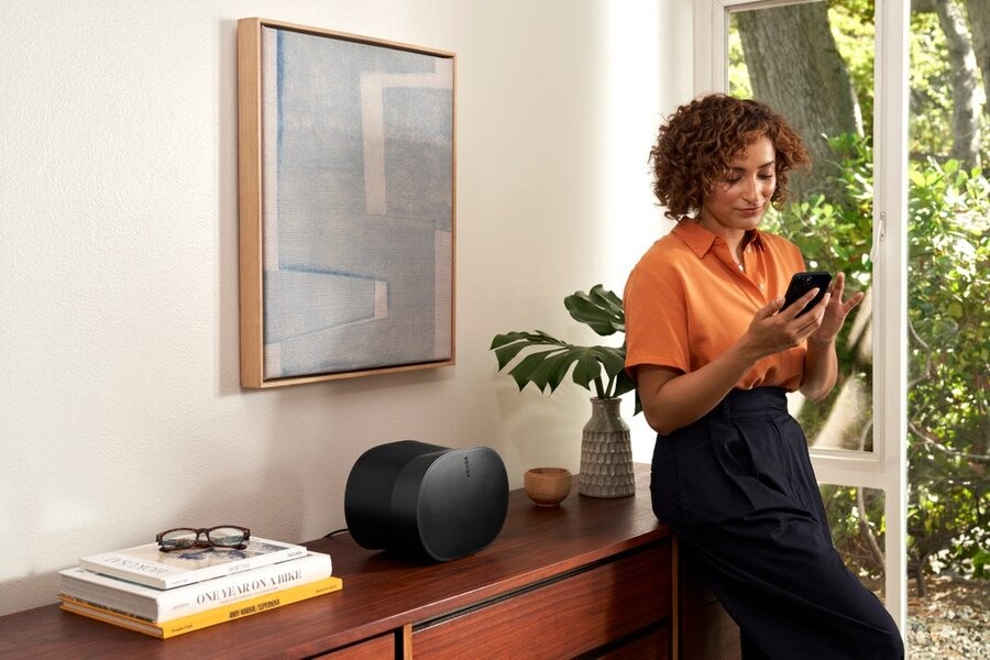 A woman using her phone near a side table with a Sonos whole-home speaker sitting on it.