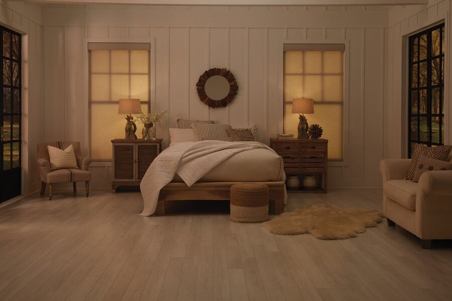 A bedroom in dimmed lighting with two windows on either side of the bed featuring closed motorized shades.