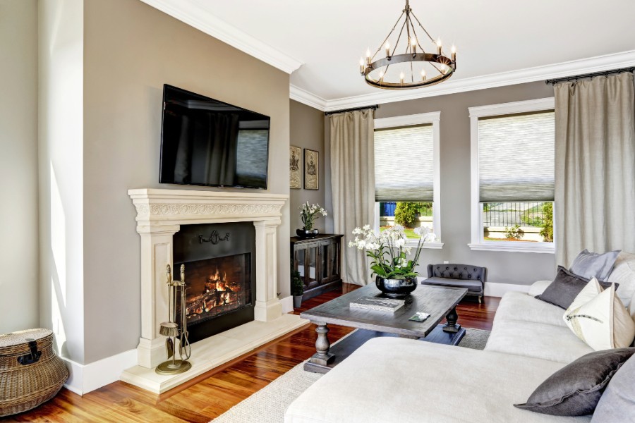 A living room featuring a fireplace under a wall-mounted TV, a sofa, a dark wood coffee table, and motorized shades. 